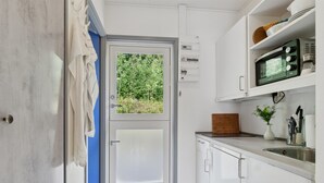 A compact kitchen with a view of greenery through a door, a microwave, and a sink.