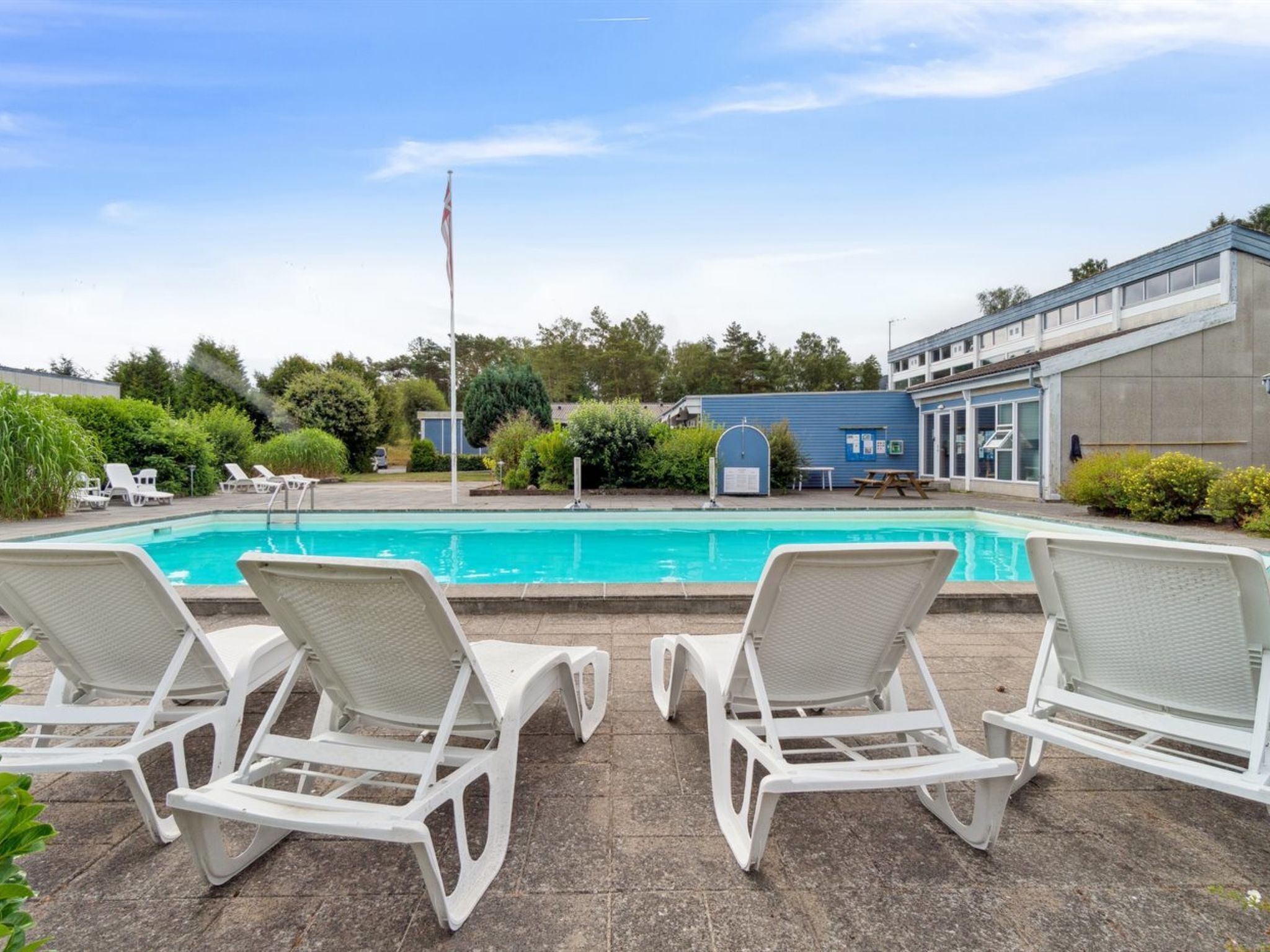 A swimming pool with lounge chairs, a flagpole, and a building with a blue exterior.