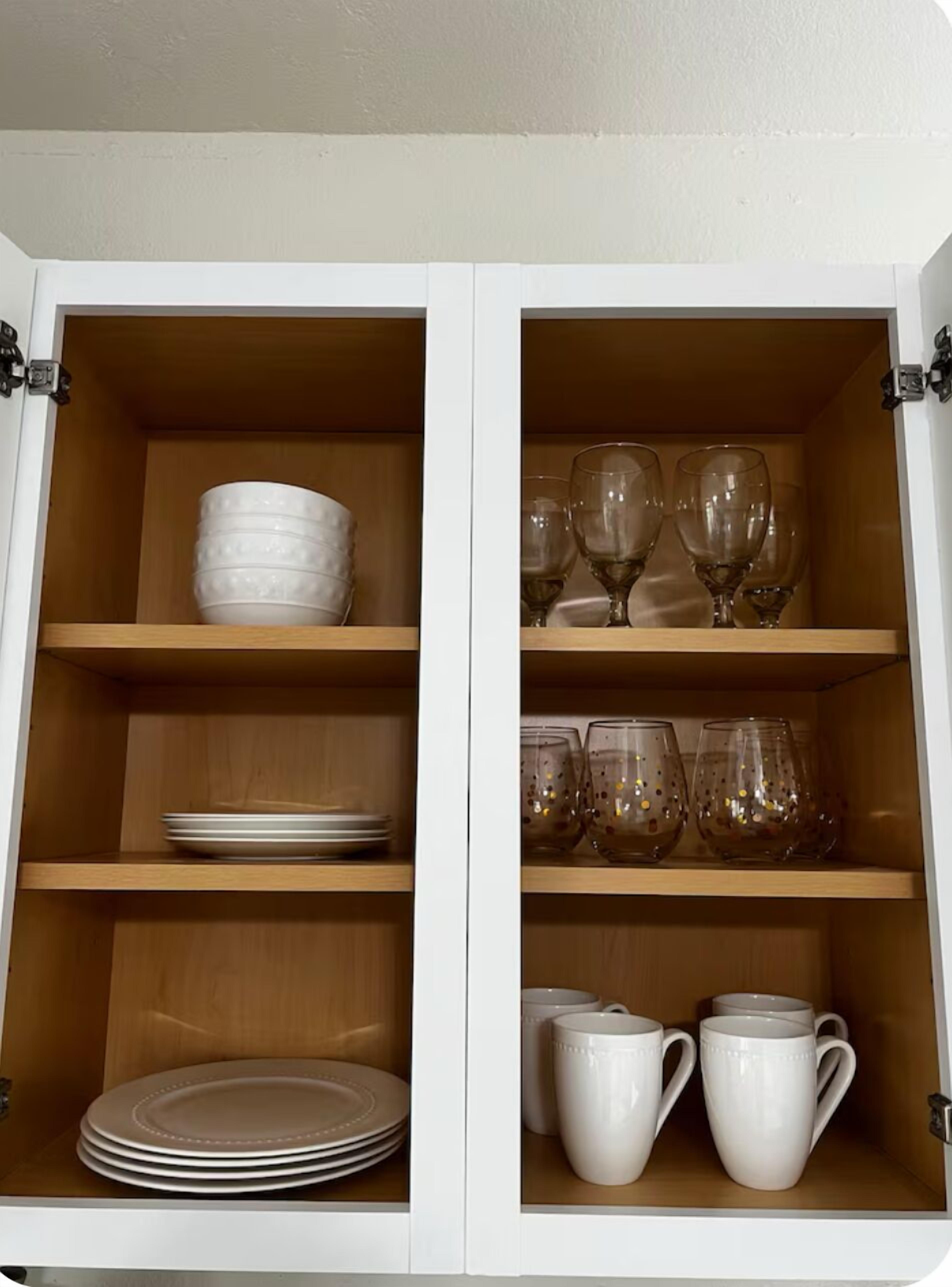 A cabinet with shelves containing plates, bowls, wine glasses, and mugs.