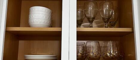 A cabinet with shelves containing plates, bowls, wine glasses, and mugs.