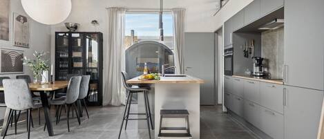 A modern kitchen with grey cabinets, a central island, and a dining area with chairs and a table.