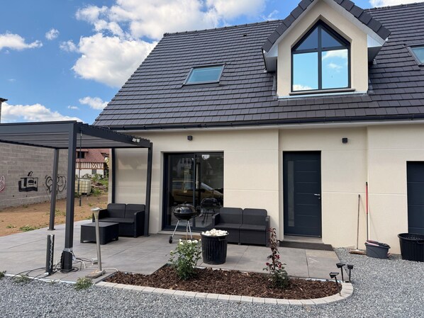Une maison moderne dotée d’un patio couvert, d’un espace salon extérieur et d’un petit jardin.