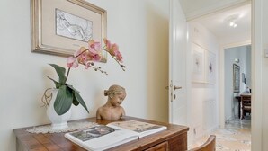 Una mesa de madera con un jarrón blanco y orquídeas rosas, un busto y un libro abierto.