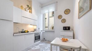 Una cocina compacta con muebles blancos, una mesa de comedor con sillas y una ventana pequeña que proporciona luz natural.