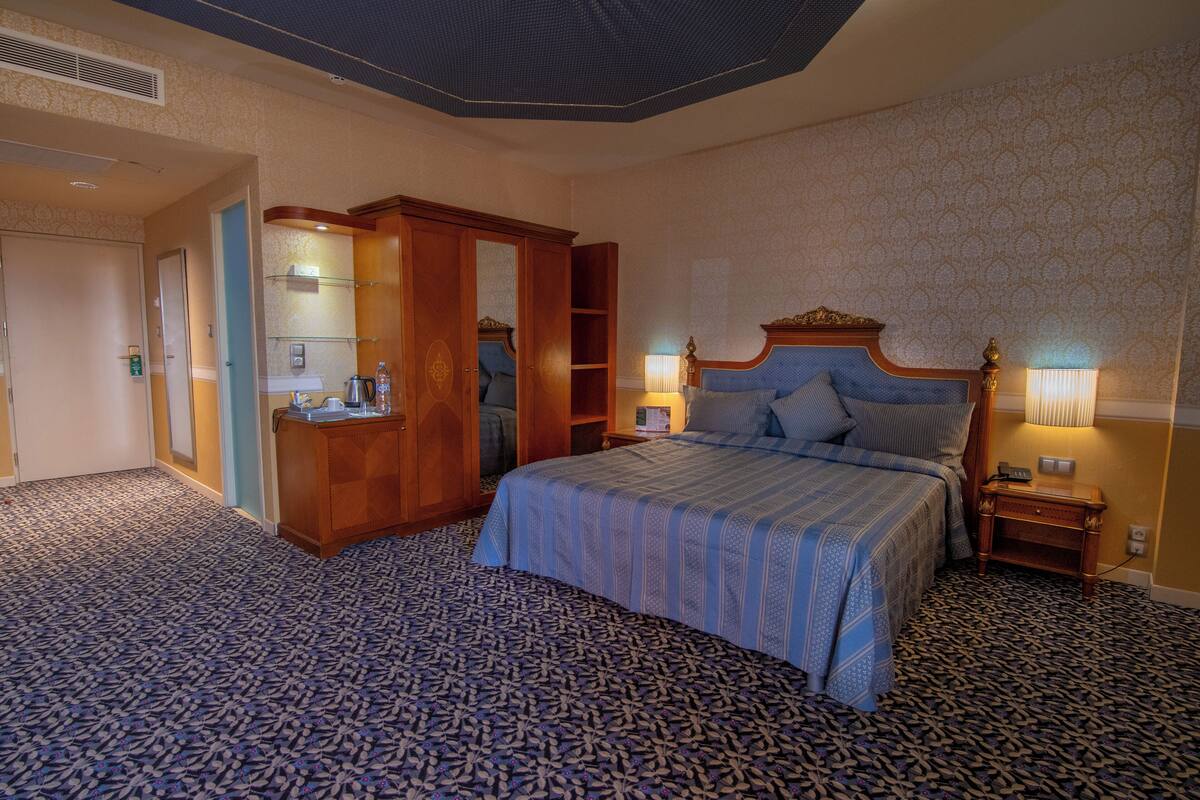 Een hotelkamer met een groot bed, een kledingkast, een bureau en een nachtkastje met lampen.