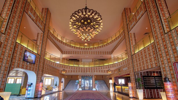 Een ruime lobby met een grote kroonluchter, meerdere verdiepingen en een centrale trap.