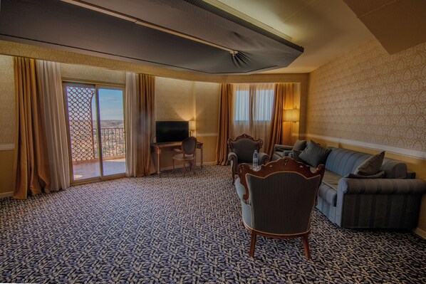 A hotel room with a large window, a television, a sofa, a chair, and a desk. - Hotel Belvedere (Bounoura)