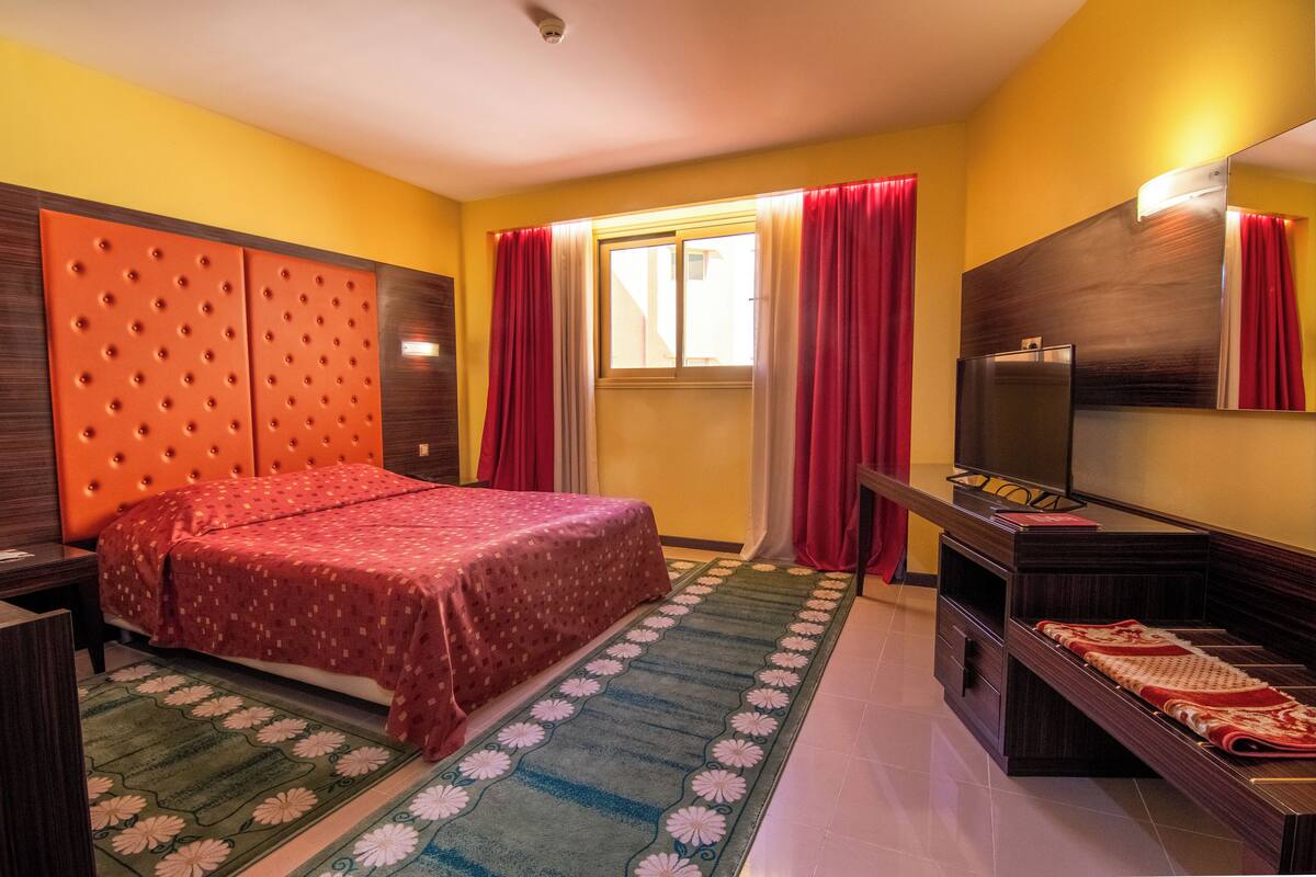 Een hotelkamer met een bed, een televisie, een bureau en een raam met gordijnen.