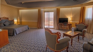 Hotelkamer met een bed, twee fauteuils, een klein tafeltje, een televisie en een groot raam met gordijnen.