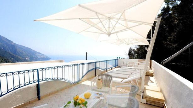 An outdoor terrace with white wicker furniture, a table with a vase of flowers, and a large white umbrella. - Villa Dei in Positano - Double Room (Positano)