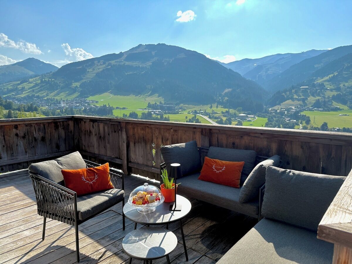 A wooden deck with outdoor furniture, a glass-top table, and a view of mountains.