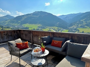 Une terrasse en bois avec des meubles dâextĂ©rieur, une table Ă plateau en verre et une vue sur les montagnes.