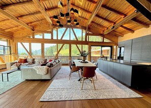 Un'ampia stanza con soffitto in legno, zona pranzo, divano e angolo cottura.