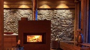Ein gemütlicher Raum mit Steinwand, Kamin und einem Holztisch mit Vase und Gläsern.