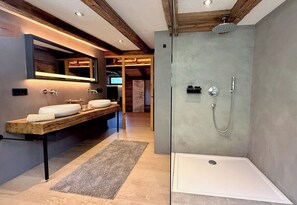 A modern bathroom with a glass-enclosed shower, a vanity with a mirror, and a bench.
