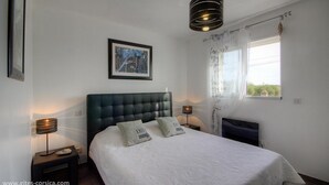 A bedroom with a large bed, two bedside tables, a framed picture on the wall, and a window with curtains.