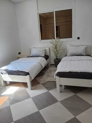A room with two beds, a window, and a potted plant.