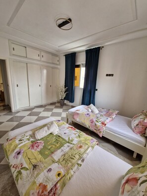 Quarto de hotel com duas camas, um guarda-roupa, um vaso de planta e chão xadrez.
