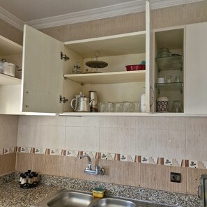 Una cocina con encimera de granito, un fregadero y un armario con distintos utensilios de cocina.