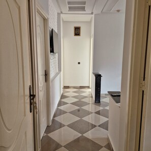 Um corredor com padrão de piso xadrez, uma porta à esquerda e um objeto pequeno e preto à direita.