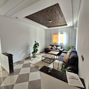 Ein modernes Wohnzimmer mit Schachbrettmuster-Boden, einer Couch, einem Couchtisch, einer Topfpflanze und einer Decke mit geometrischem Muster.