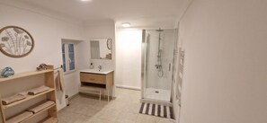 Une salle de bain avec une douche, un lavabo, un miroir et une étagère avec des serviettes.