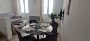 A dining area with a round table set for four, a sofa, a potted plant, and a wall-mounted TV.