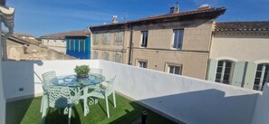 Un balcon avec une table et des chaises en verre, une petite plante en pot et une vue sur les immeubles voisins.