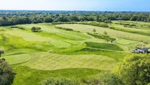 Hyvin hoidettu golfkenttä, jossa on siistit viheriöt ja väylät, ja jota ympäröivät tiheät puut sekä kaupungin siluetti, joka näkyy kauempana.