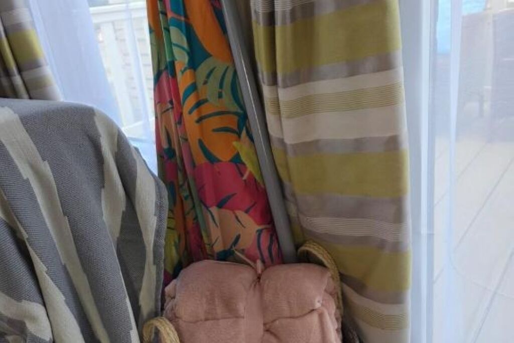 A room with a window covered by curtains, a bed with a striped blanket, and a pink pillow.