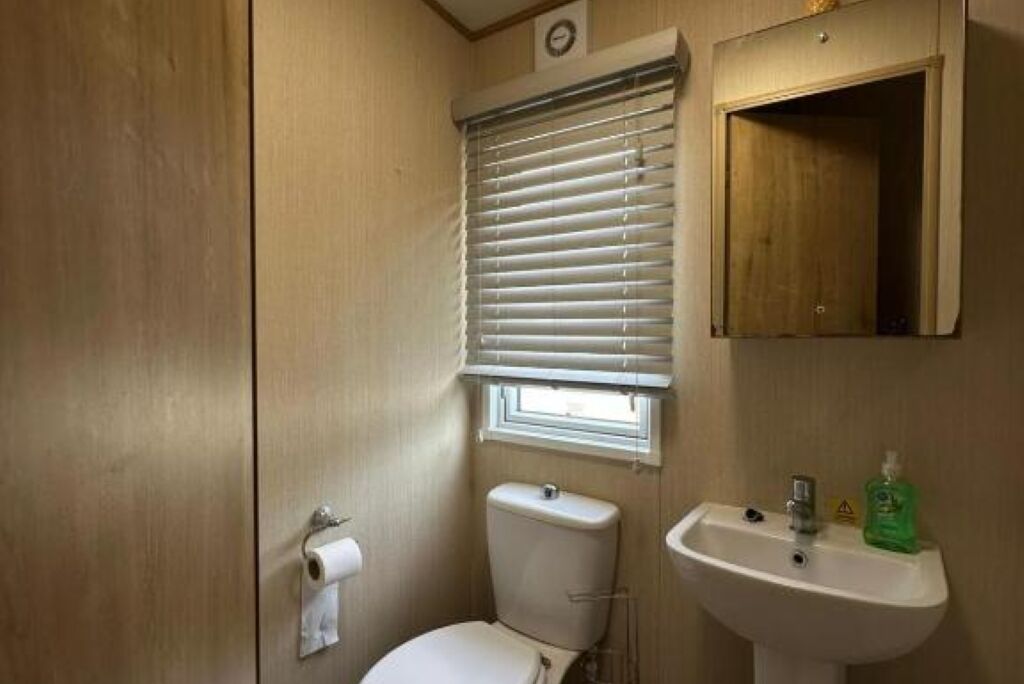 Un baño pequeño y funcional con inodoro, lavamanos y ventana con persianas.