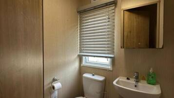 Un baño pequeño y funcional con inodoro, lavamanos y ventana con persianas.