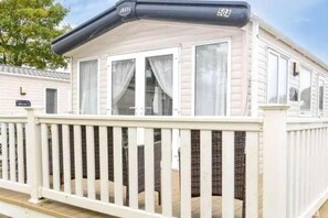 Een stacaravan met een witte buitenkant, een terras met witte relingen en een zwarte dakventilatie met de aanduiding 'ABI 50A'.