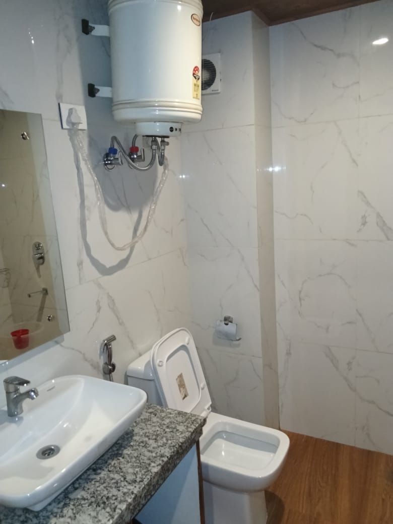 Een badkamer met een marmeren wand, een wastafel, een toilet en een aan de wand bevestigde boiler.