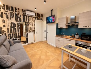 A modern kitchen with a flat-screen TV, wooden cabinets, and a dining area with a table and chairs. - Centro & Mare - Rooms & Suites (Termoli)