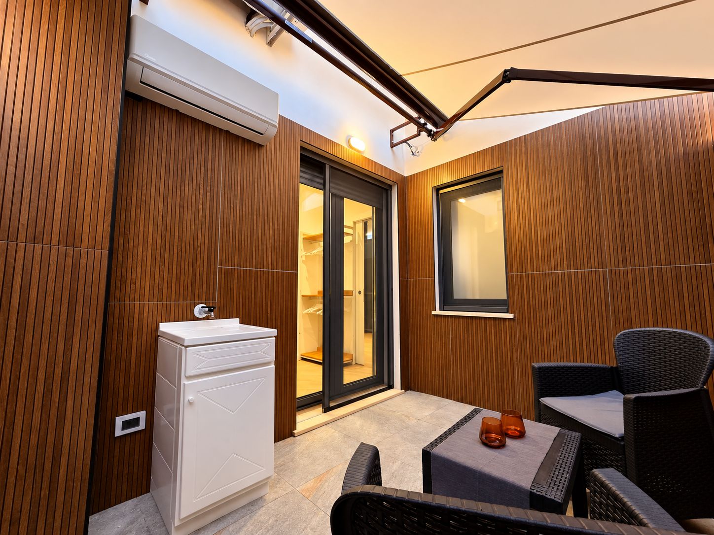 Un baño moderno con un lavabo blanco, paneles de madera y una puerta de cristal que da a la zona de la ducha.