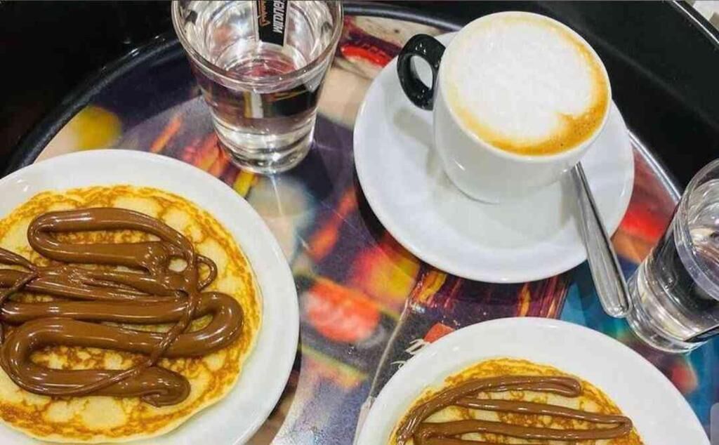 A tray with two plates of pancakes topped with chocolate sauce, a cup of coffee, and a glass of water.
