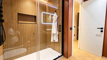Habitación de hotel con puerta corrediza de vidrio, pared de paneles de madera, bata blanca colgada en la puerta y puerta blanca que conduce a otra habitación.