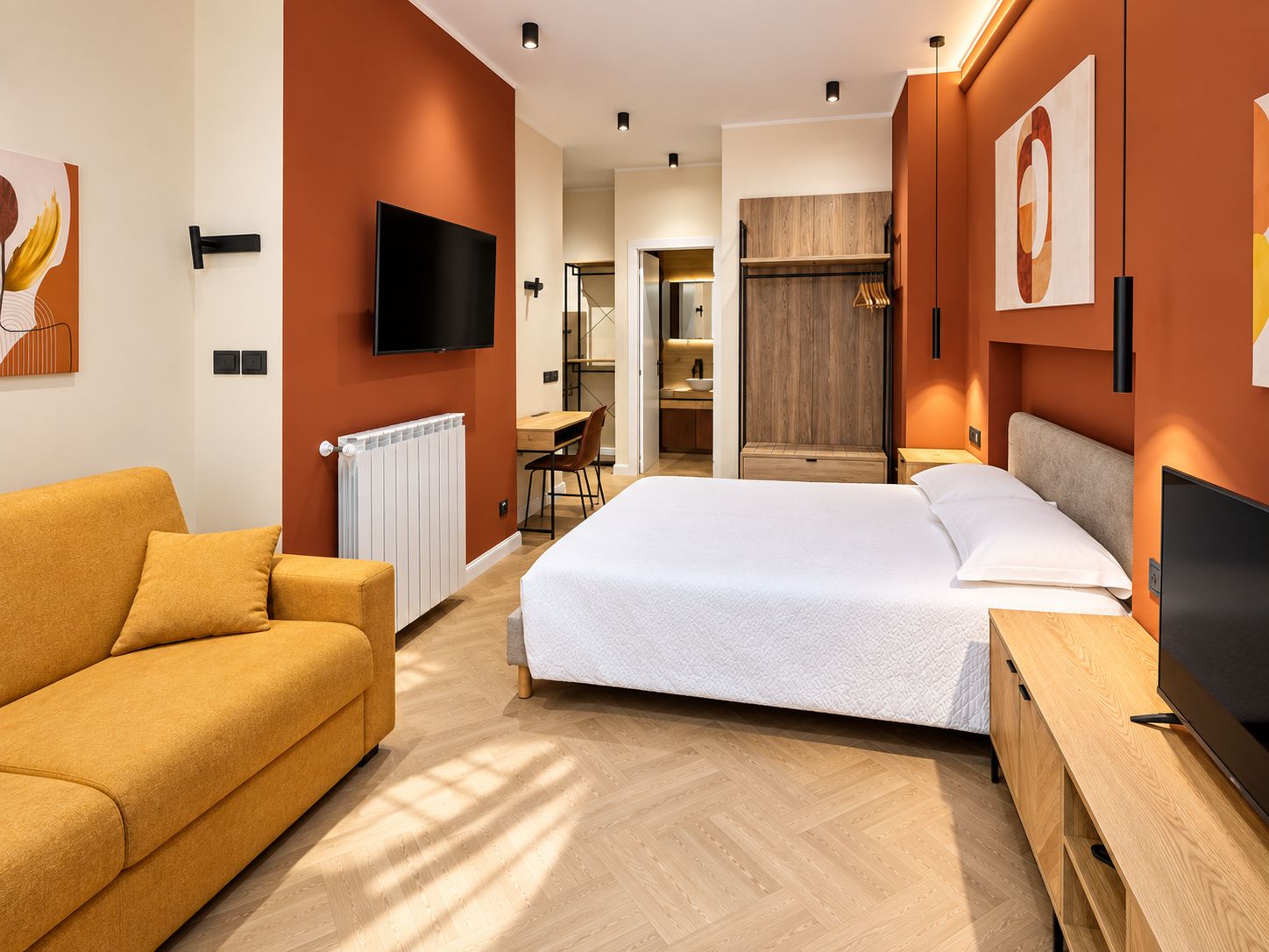 A modern hotel room with a bed, a sofa, a TV, and a desk.