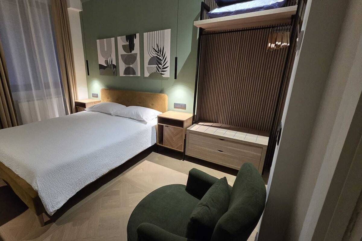 A hotel room with a bed, bedside tables, a chair, and artwork on the wall.