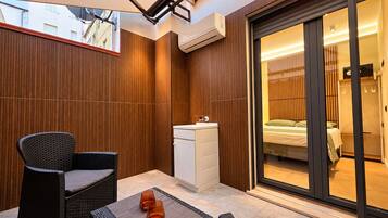 A modern outdoor seating area with a table and chairs, an air conditioning unit, and a sliding glass door leading to a bedroom.