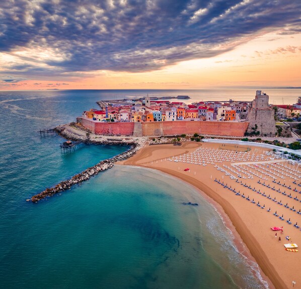A coastal town with a fortified wall, a sandy beach with umbrellas, and a clear view of the sea. - Centro & Mare - Rooms & Suites (Termoli)