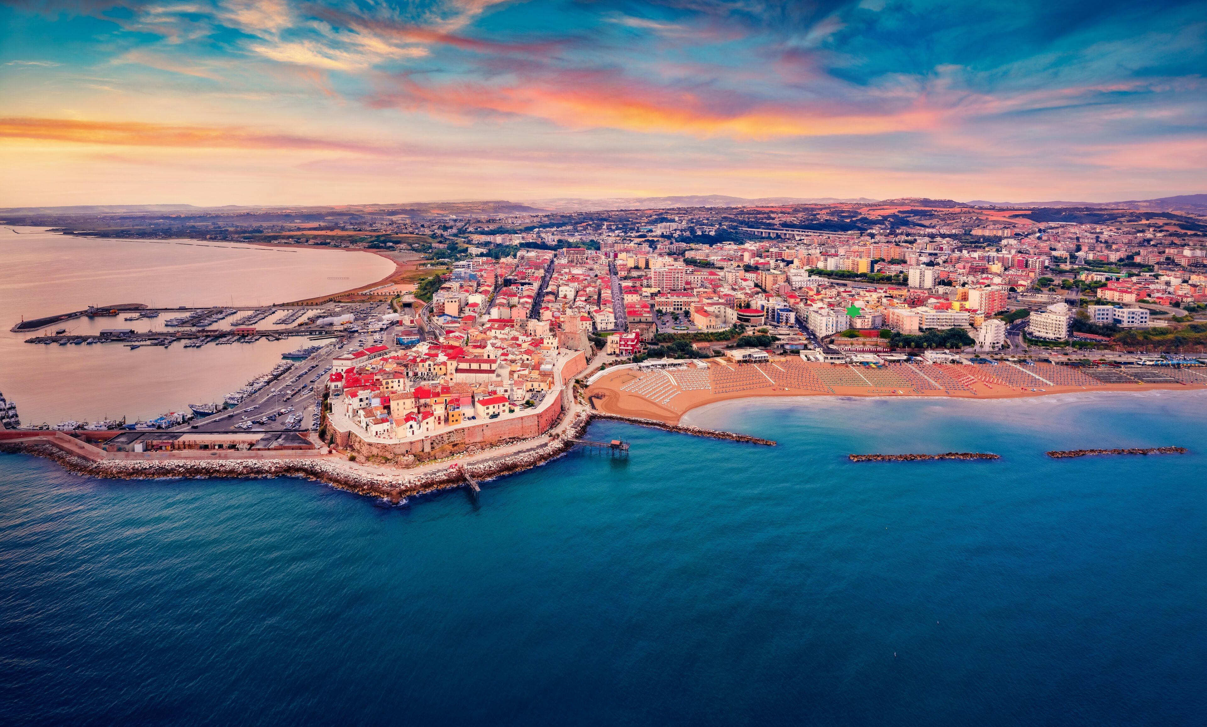 Vista aérea de una ciudad costera con una fortaleza destacada, un puerto deportivo y una amplia zona de playa.