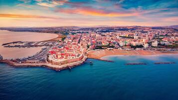 Vista aérea de una ciudad costera con una fortaleza destacada, un puerto deportivo y una amplia zona de playa.