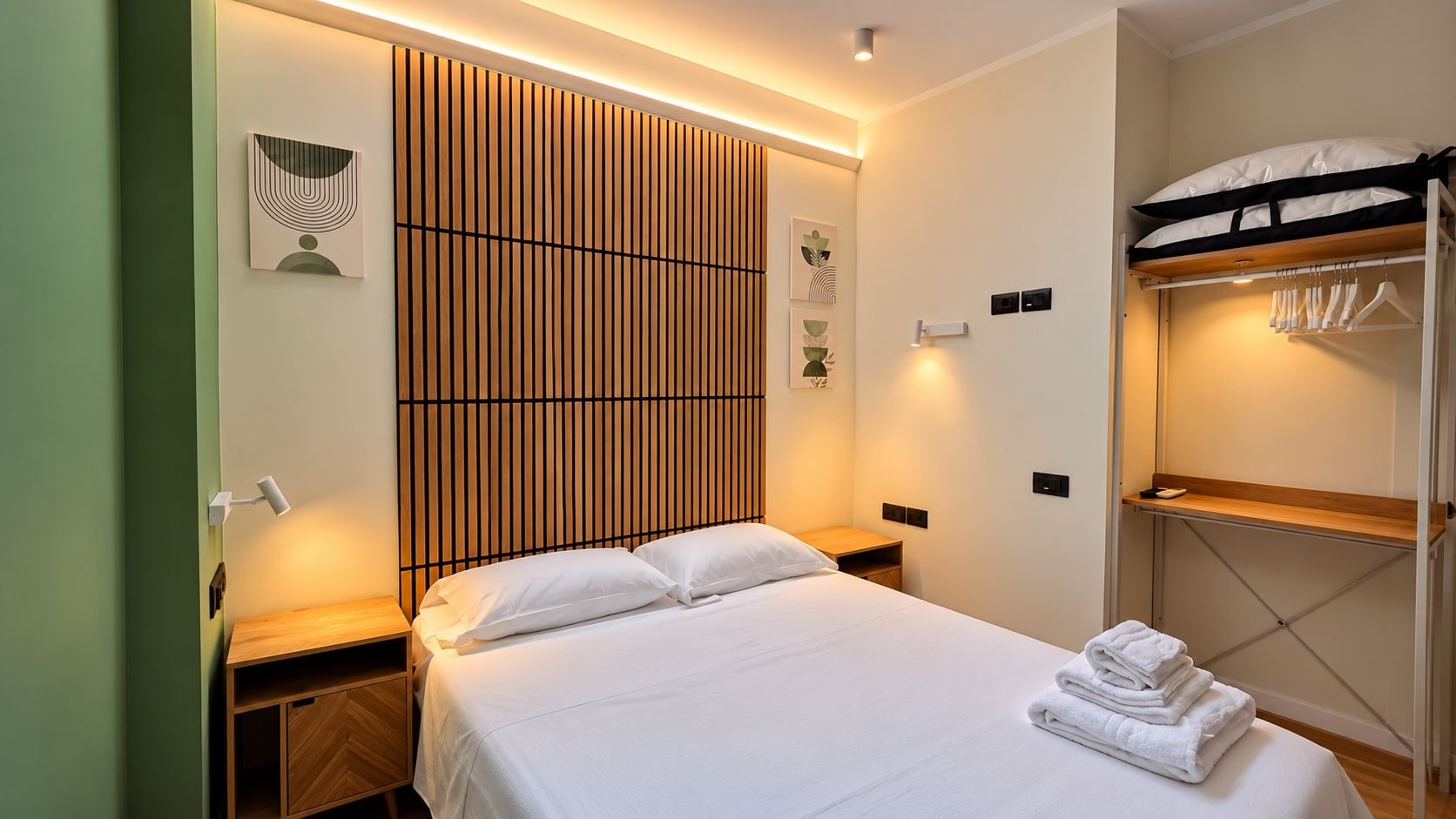 A hotel room with a bed, bedside tables, a wardrobe, and a wall-mounted light fixture.