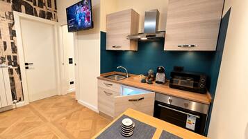 Una cocina compacta con microondas, tostadora y cafetera en la encimera, un lavabo e incluso alacenas superiores.