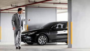 Un hombre con traje señala un coche negro en un estacionamiento.