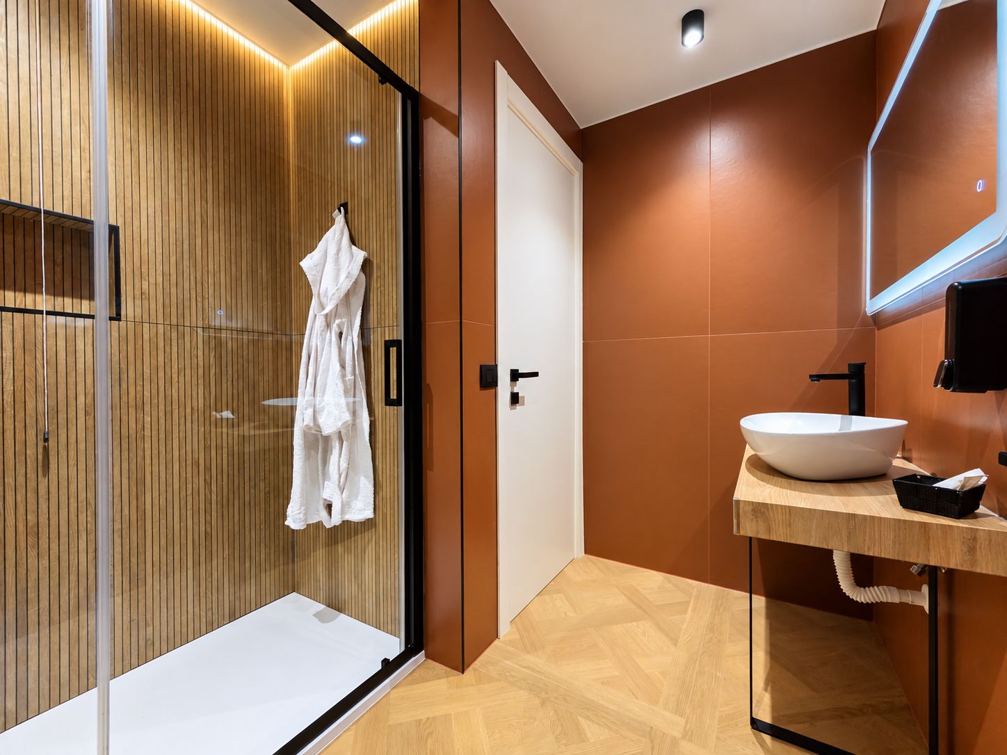 Un baño moderno con cabina de ducha de vidrio, un lavabo blanco y un mueble de tocador de madera.