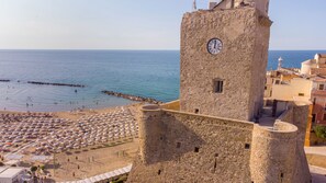 A coastal town with a prominent stone tower featuring a clock, a beach with umbrellas, and a clear view of the sea. - Centro & Mare - Rooms & Suites (Termoli)