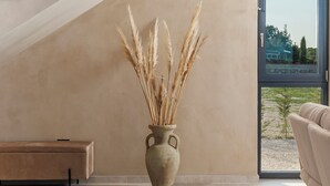 Un interior moderno con una escalera, un ventanal grande y un florero con plantas secas.